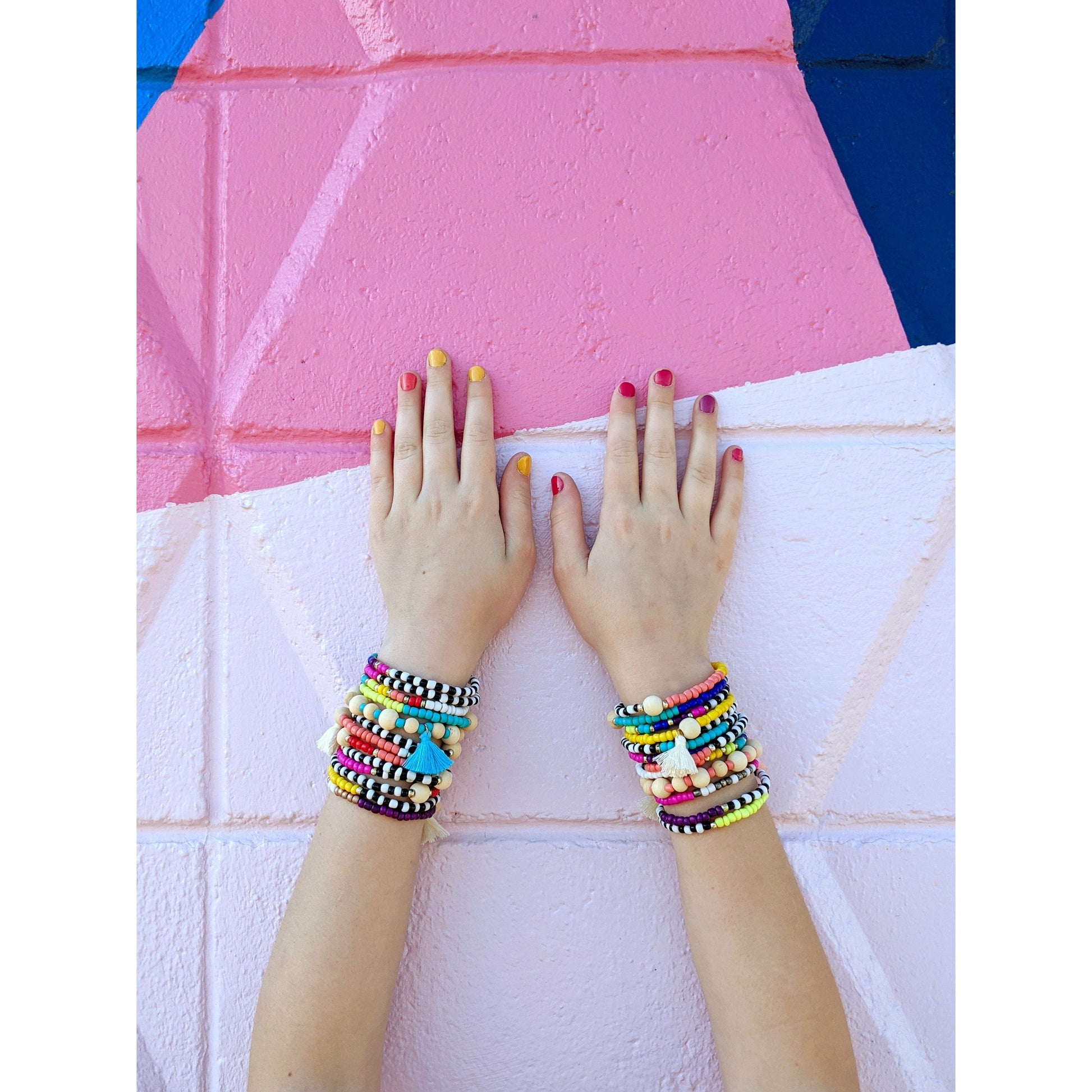 image shows two arms stretched up a wall with multiple, colourful, beaded bracelets on eaxh wrist